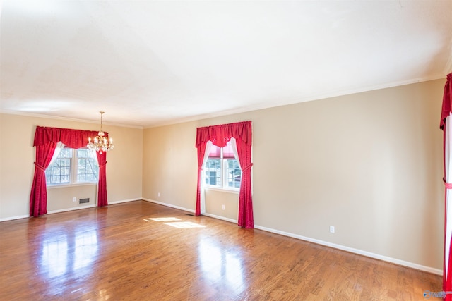 empty room with wood-type flooring, a chandelier, and crown molding