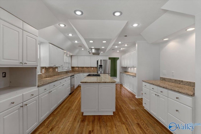 kitchen featuring sink, white cabinetry, light stone counters, appliances with stainless steel finishes, and a kitchen island