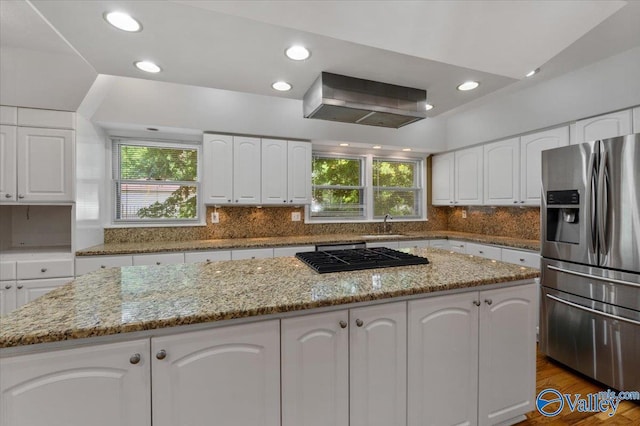 kitchen featuring white cabinetry, a center island, stainless steel refrigerator with ice dispenser, light stone countertops, and black gas stovetop