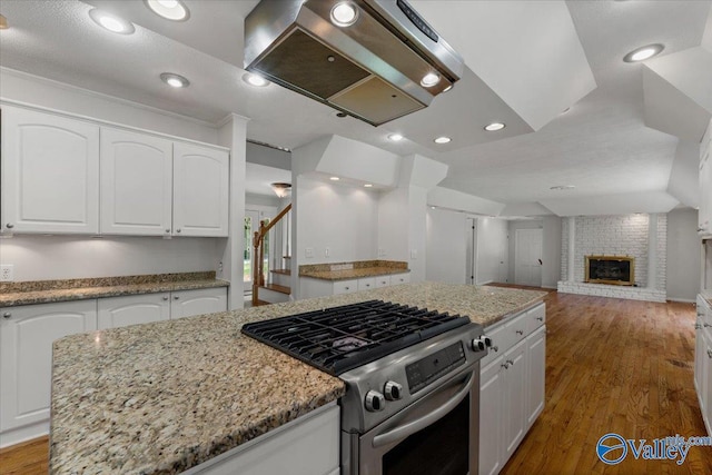 kitchen featuring stainless steel range with gas cooktop, island range hood, a kitchen island, and white cabinets