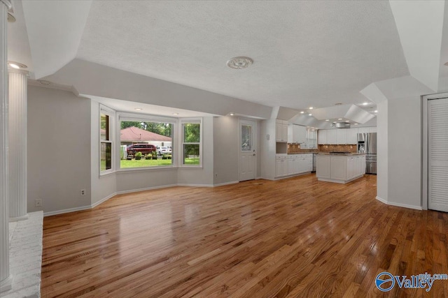 unfurnished living room with vaulted ceiling, a textured ceiling, and light hardwood / wood-style floors