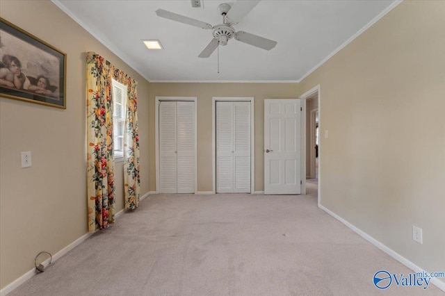 unfurnished bedroom with crown molding, light colored carpet, ceiling fan, and two closets