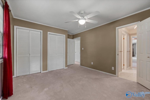 unfurnished bedroom featuring ceiling fan, ornamental molding, light colored carpet, and multiple closets