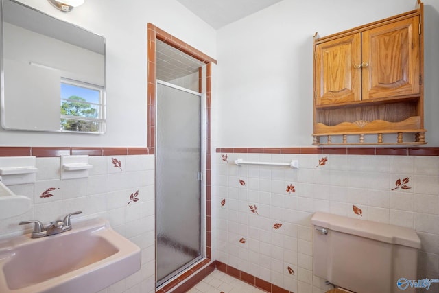 full bath featuring a stall shower, toilet, a wainscoted wall, a sink, and tile walls