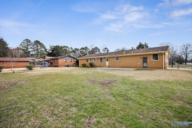 back of house featuring fence, a lawn, a playground, and brick siding