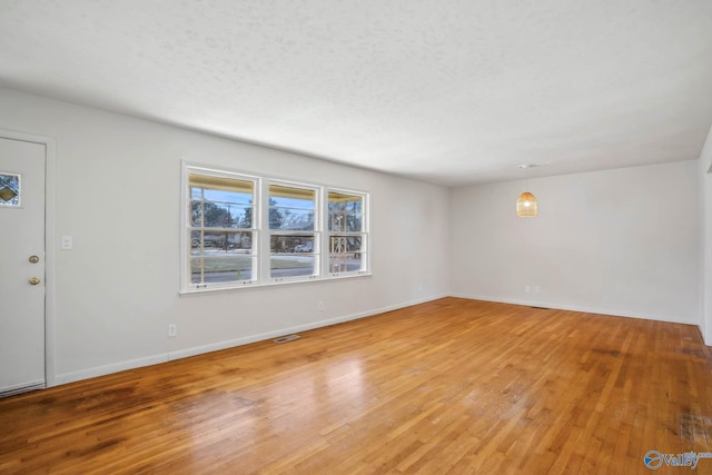 unfurnished living room featuring visible vents, a textured ceiling, baseboards, and hardwood / wood-style flooring