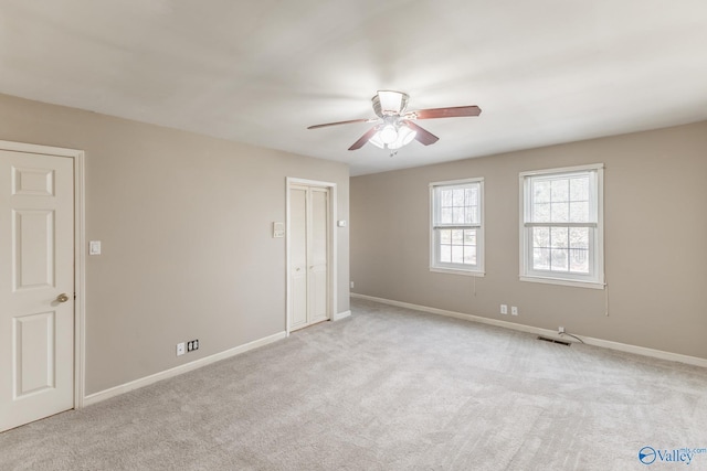 carpeted spare room with visible vents, baseboards, and ceiling fan