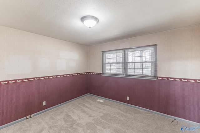 spare room with carpet flooring, a textured ceiling, wallpapered walls, and baseboards