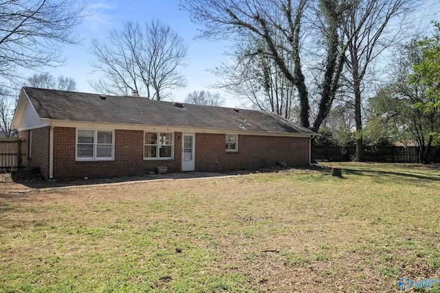 back of house featuring brick siding, a lawn, and fence