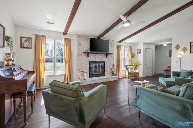 living room featuring wood finished floors, visible vents, vaulted ceiling with beams, ceiling fan, and a stone fireplace