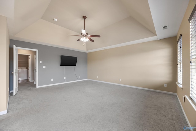 unfurnished living room with light carpet, washer / dryer, a raised ceiling, and ceiling fan