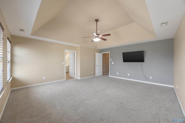 interior space with a raised ceiling, light colored carpet, and ceiling fan