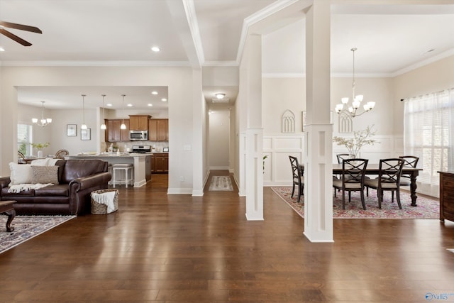 living area with dark wood-style floors, crown molding, and ceiling fan with notable chandelier