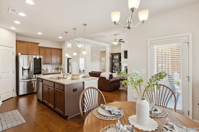 kitchen featuring light stone countertops, dark wood finished floors, ceiling fan with notable chandelier, appliances with stainless steel finishes, and a sink