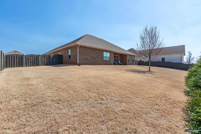 back of house featuring brick siding, a lawn, and fence