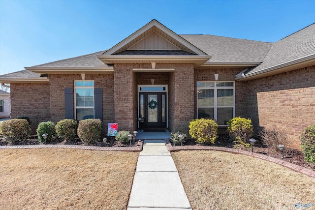 view of front of property featuring brick siding, roof with shingles, and a front yard