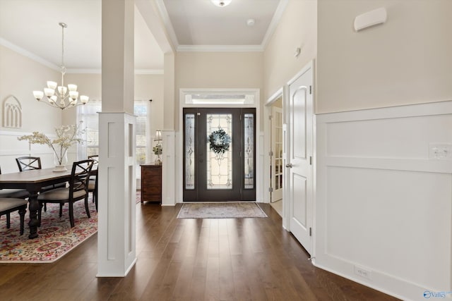 foyer featuring dark wood finished floors, an inviting chandelier, wainscoting, crown molding, and a decorative wall