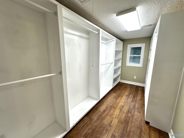 spacious closet featuring dark wood finished floors, visible vents, and attic access