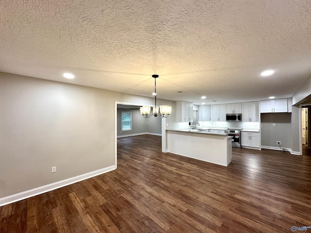 kitchen with dark wood-style floors, a peninsula, white cabinets, appliances with stainless steel finishes, and a notable chandelier