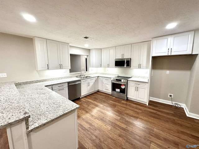 kitchen featuring stainless steel appliances, light stone counters, dark hardwood / wood-style flooring, kitchen peninsula, and white cabinets