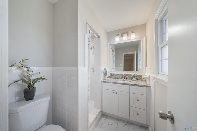 bathroom with marble finish floor, tile walls, toilet, wainscoting, and vanity