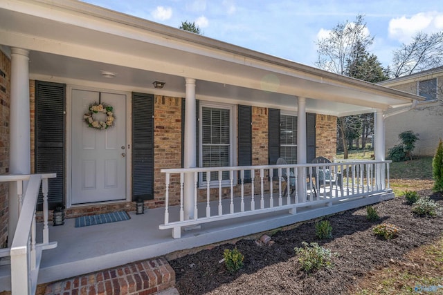 doorway to property featuring a porch and brick siding