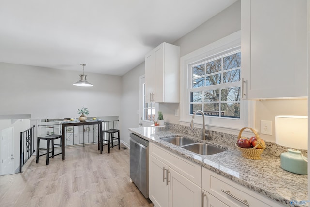 kitchen with light stone counters, light wood finished floors, stainless steel dishwasher, white cabinetry, and a sink