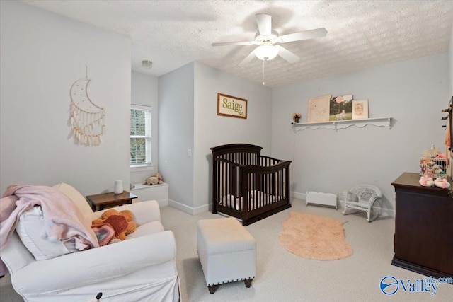 bedroom featuring ceiling fan, a crib, a textured ceiling, and light carpet