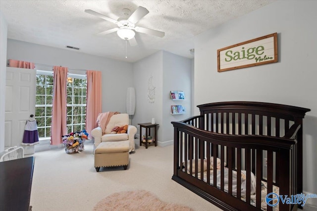 bedroom featuring carpet, a textured ceiling, a nursery area, and ceiling fan