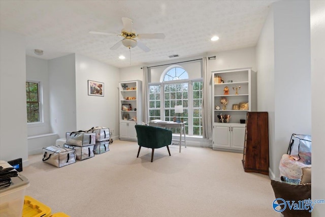 living area with a textured ceiling, light colored carpet, and ceiling fan