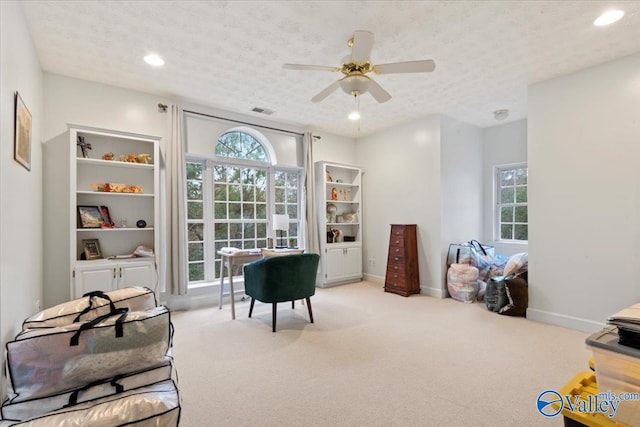 recreation room featuring a textured ceiling, light colored carpet, and ceiling fan