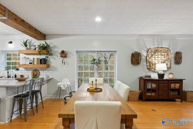 dining space featuring beamed ceiling, light wood-type flooring, and crown molding