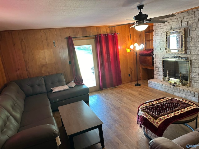 living room featuring a large fireplace, a textured ceiling, wood walls, wood-type flooring, and ceiling fan