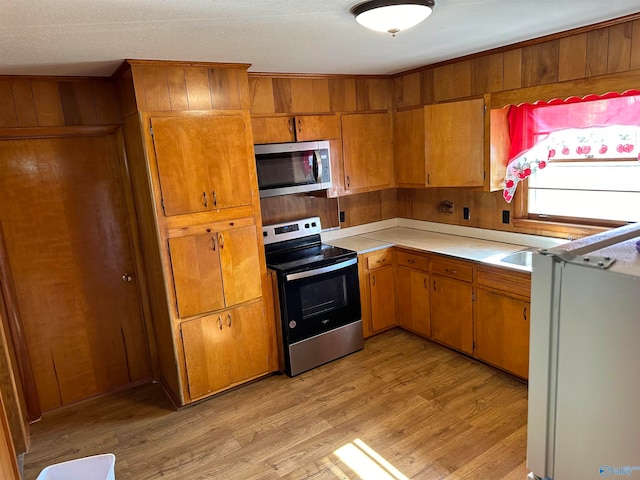 kitchen featuring wood walls, stainless steel appliances, a textured ceiling, and light hardwood / wood-style flooring