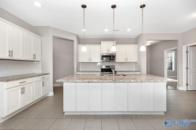 kitchen featuring a kitchen island with sink, a sink, white cabinets, appliances with stainless steel finishes, and decorative light fixtures
