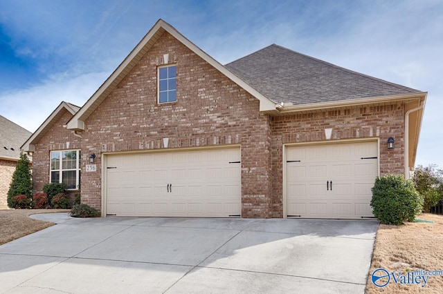 view of front of home with an attached garage, a shingled roof, concrete driveway, and brick siding