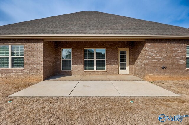 rear view of house with a shingled roof, a patio, and brick siding