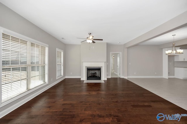 unfurnished living room with a fireplace with flush hearth, wood finished floors, baseboards, and ceiling fan with notable chandelier
