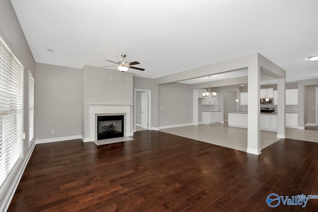 unfurnished living room featuring ceiling fan with notable chandelier, wood finished floors, a fireplace with flush hearth, and baseboards