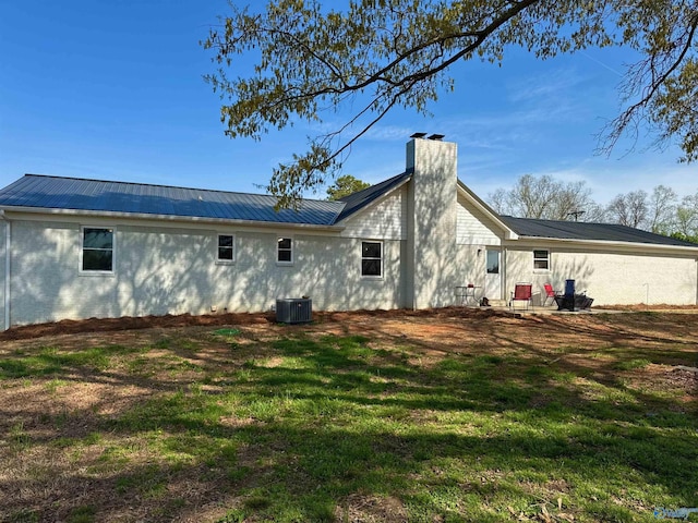 rear view of house with metal roof, a chimney, central AC, and a yard