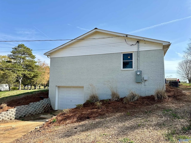 view of side of home featuring driveway, an attached garage, cooling unit, and brick siding