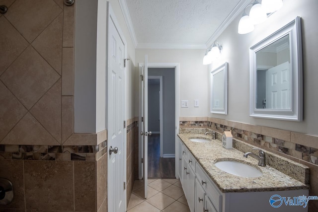 bathroom featuring tile patterned floors, ornamental molding, vanity, a textured ceiling, and tile walls