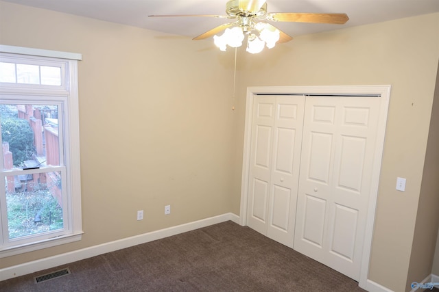 unfurnished bedroom featuring dark colored carpet, ceiling fan, multiple windows, and a closet