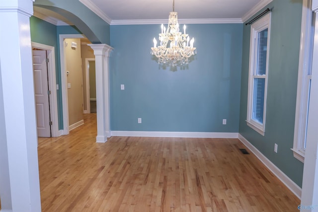 empty room featuring a chandelier, light hardwood / wood-style flooring, ornate columns, and crown molding