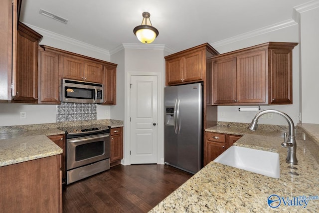 kitchen with sink, ornamental molding, appliances with stainless steel finishes, light stone countertops, and dark hardwood / wood-style flooring