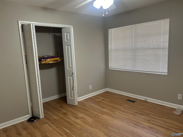 unfurnished bedroom with a textured ceiling, light wood-type flooring, a closet, and ceiling fan