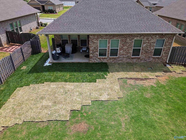 rear view of property featuring a patio, a fenced backyard, roof with shingles, brick siding, and a yard