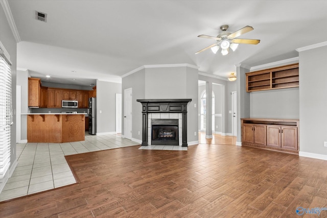 unfurnished living room featuring a healthy amount of sunlight, crown molding, ceiling fan, a fireplace, and light hardwood / wood-style floors