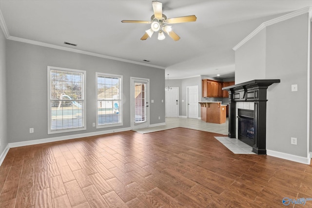 unfurnished living room with a tiled fireplace, ceiling fan, crown molding, and light wood-type flooring