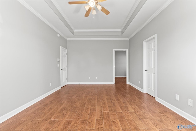 empty room with ceiling fan, a raised ceiling, light wood-type flooring, and ornamental molding